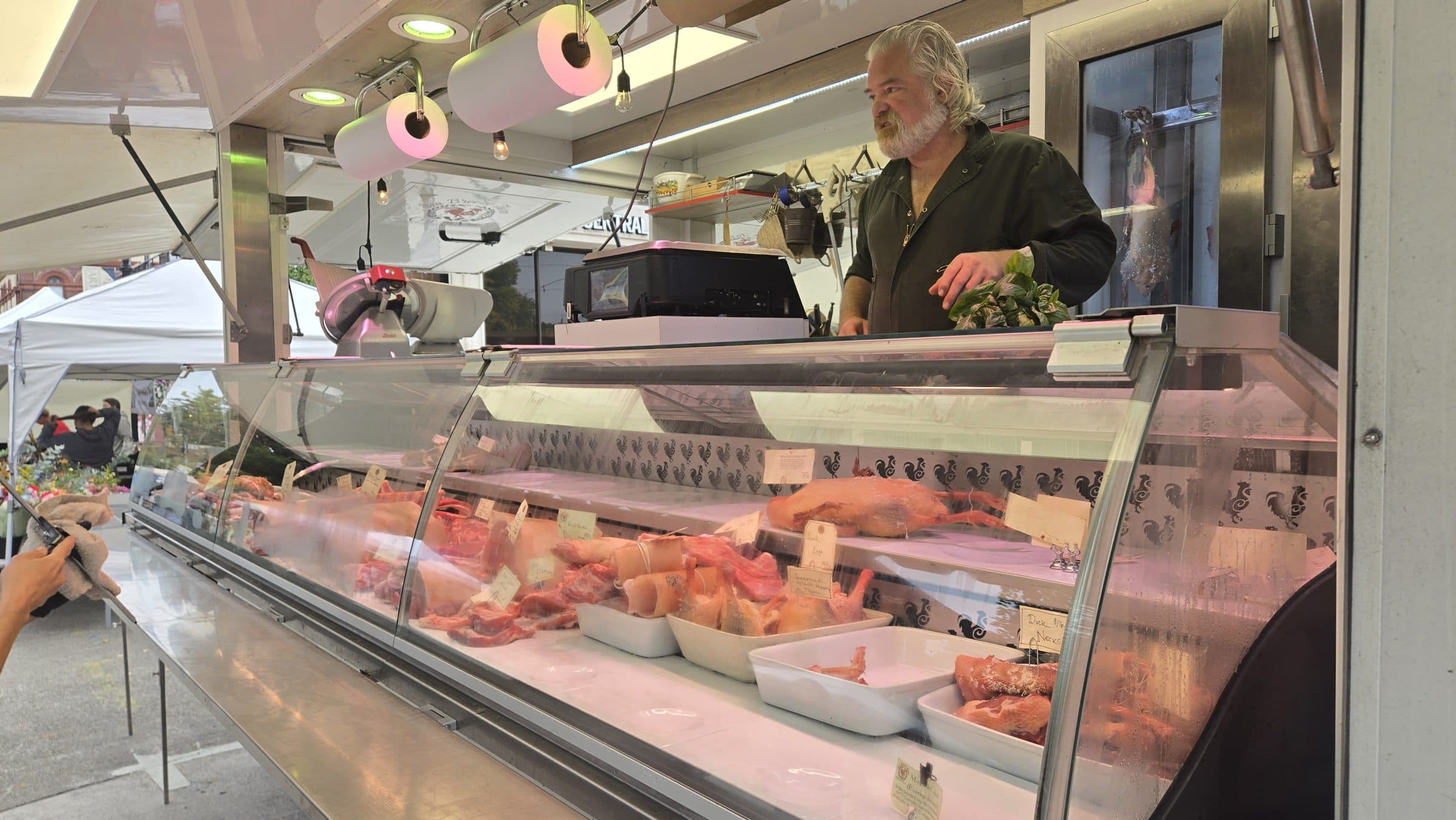 A Sea Breeze Farm vendor behind a glass case of pork and poultry at the Hillsboro Farmers Market